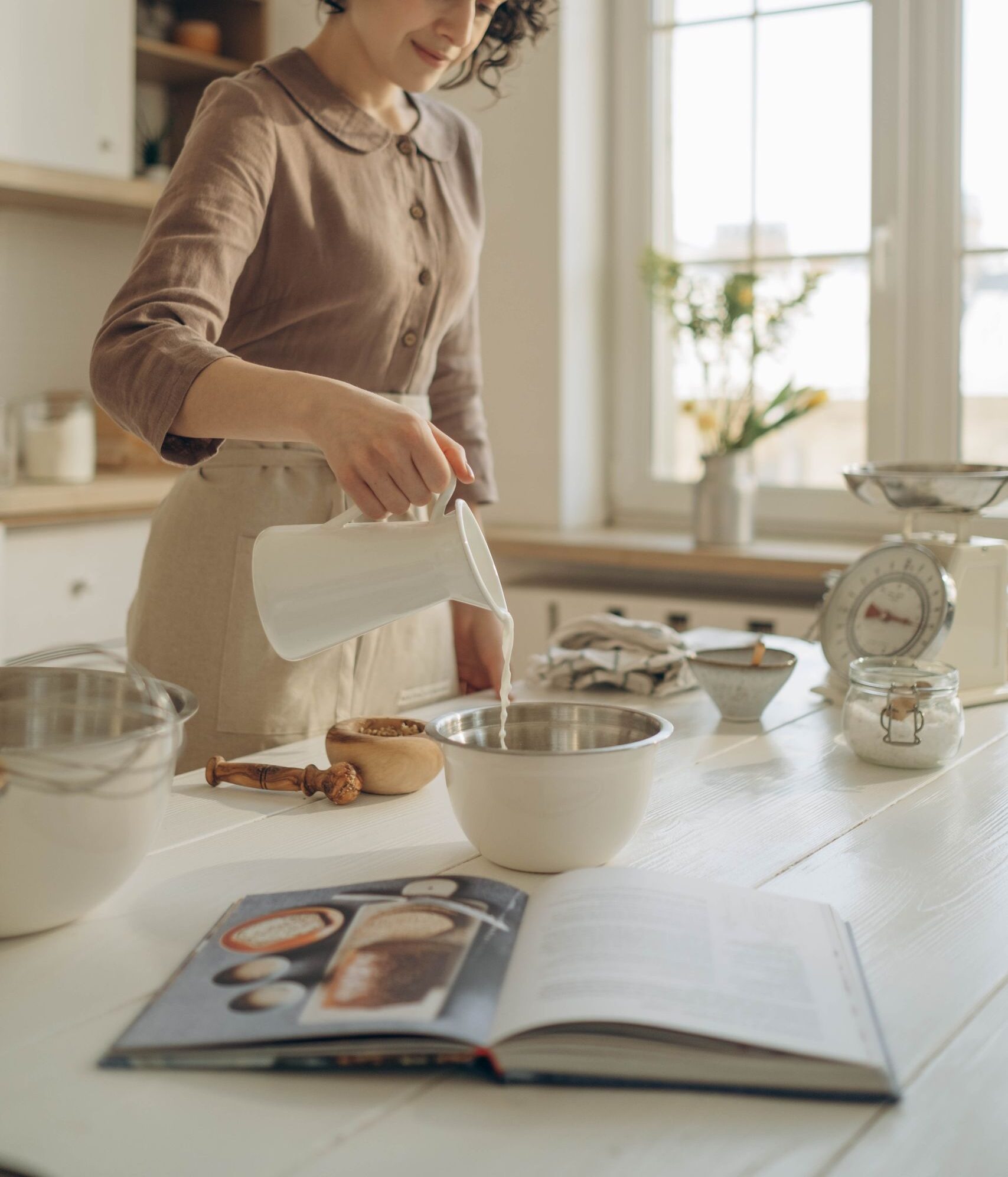 A woman preparing ingredients for baking, pouring milk into a bowl on a bright kitchen island.